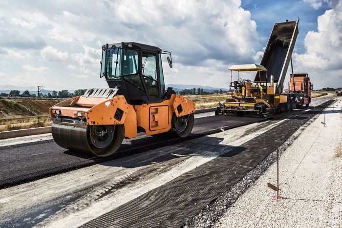 A road is being paved with a roller and a dump truck.