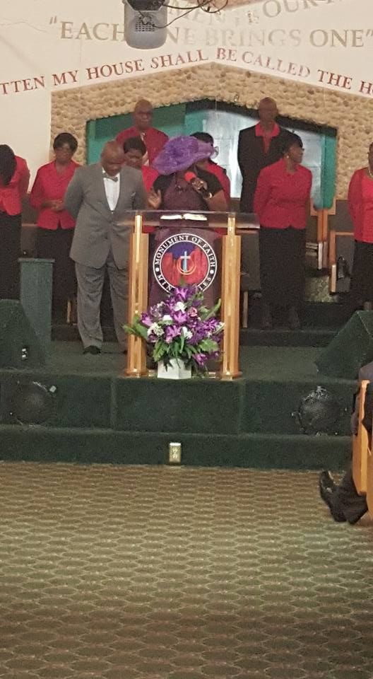 Church service: preacher at pulpit, choir in red. Flowers, gold accents, green stage.