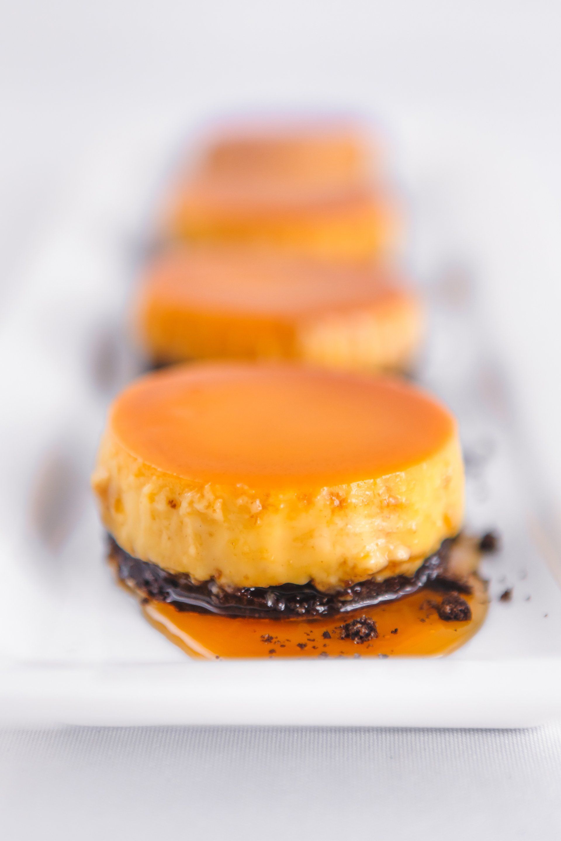 A row of flan desserts on a white plate on a table.