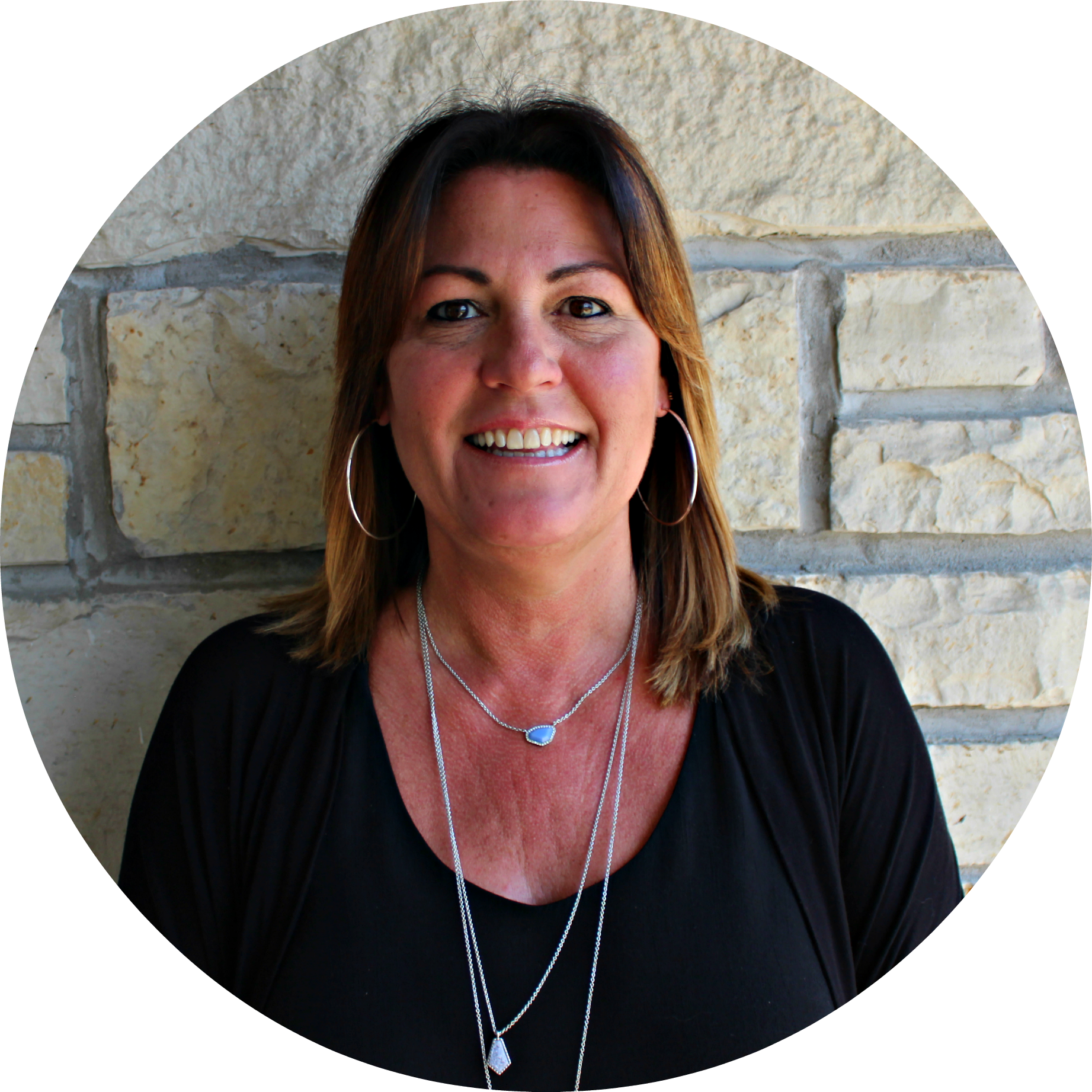 A woman in a black shirt is smiling in front of a stone wall