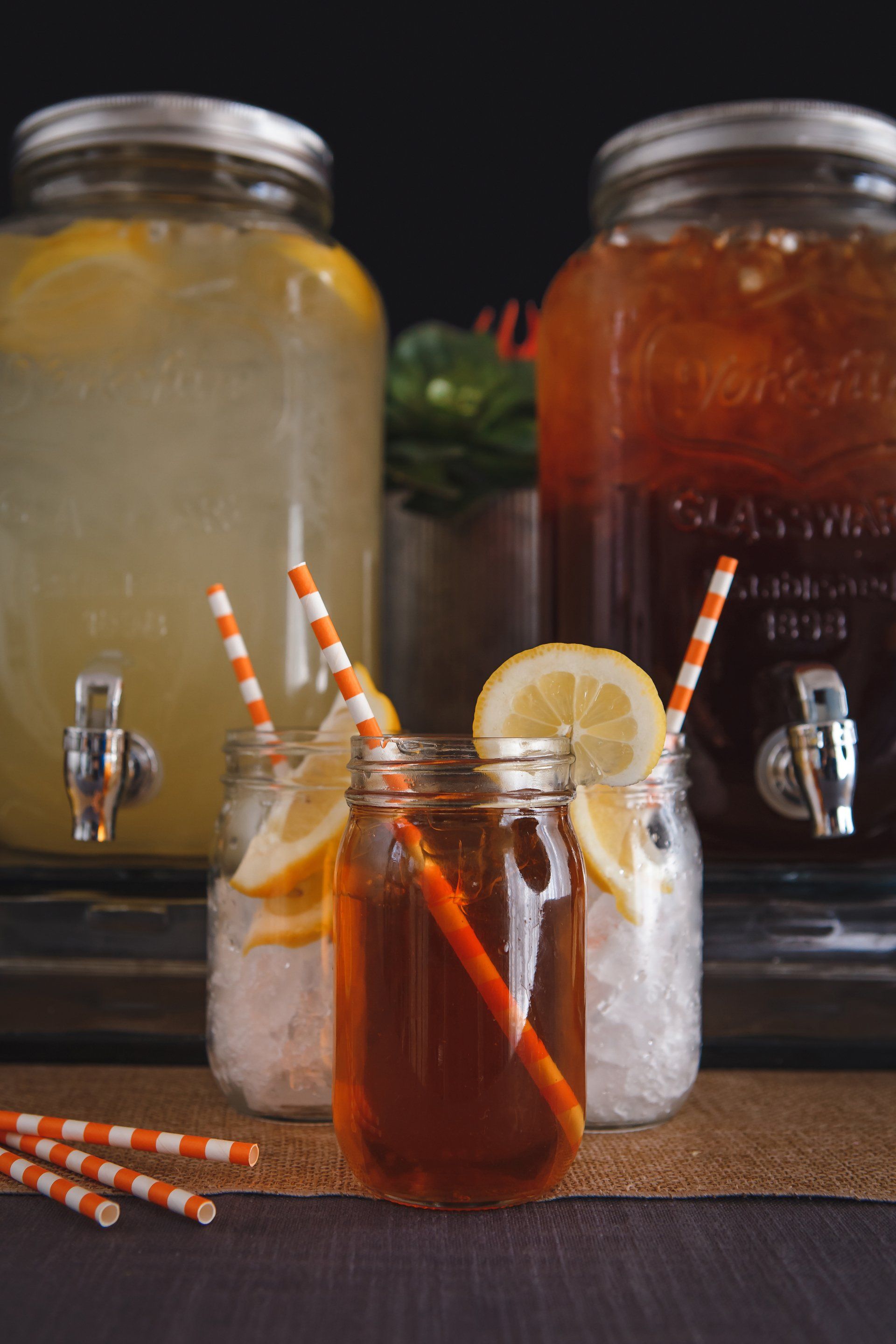 A mason jar filled with iced tea and lemon slices next to two beverage dispensers.
