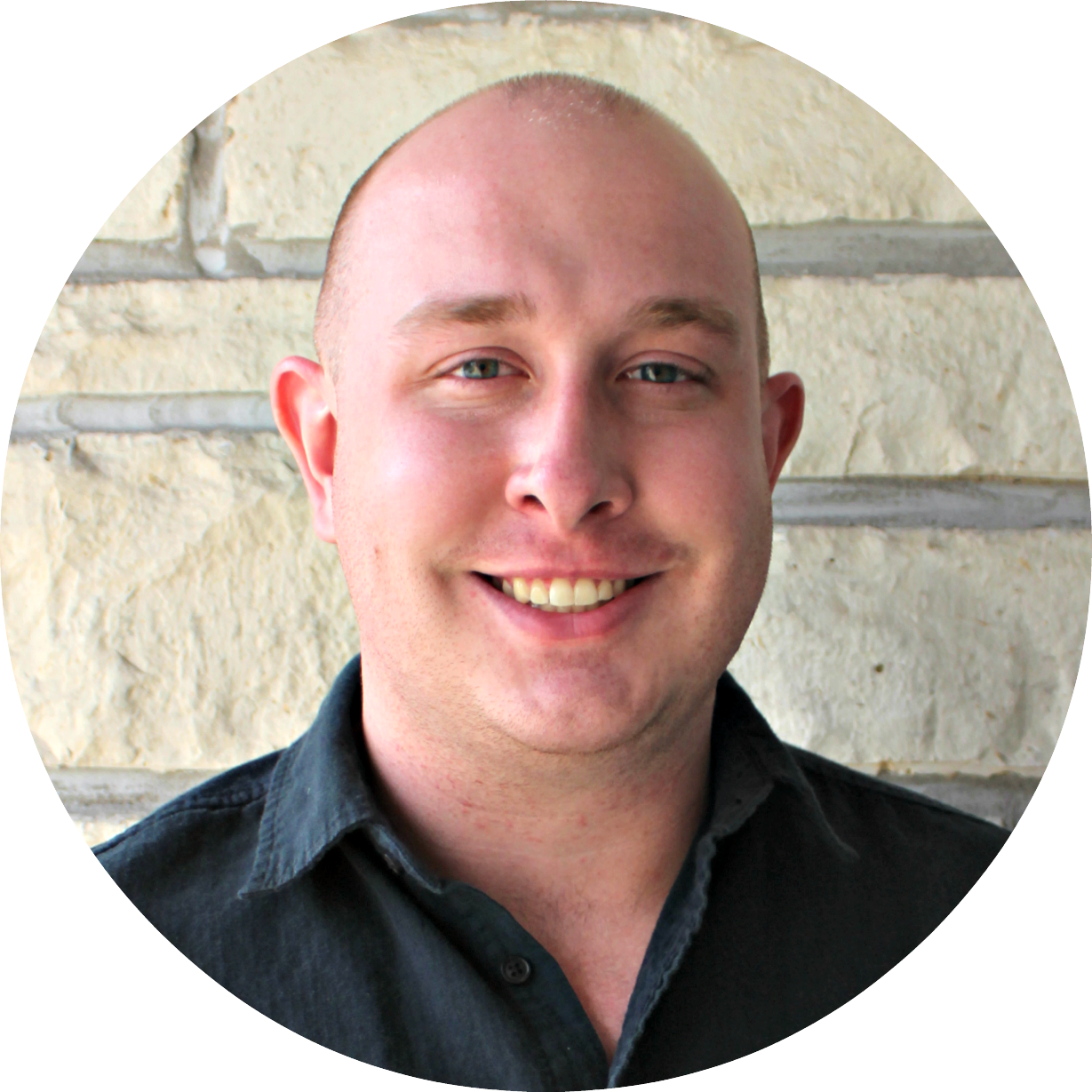 A bald man is smiling in front of a stone wall