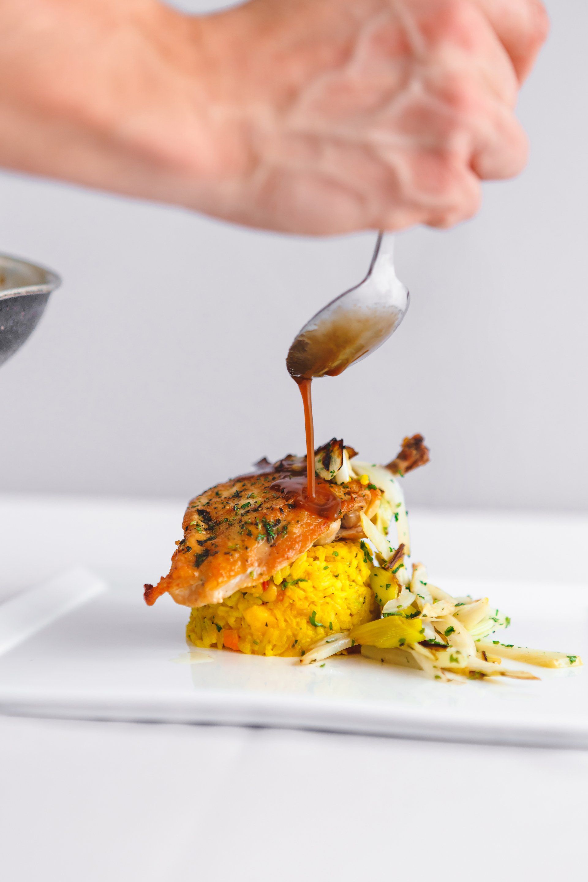 A person is pouring sauce on a plate of food with a spoon.