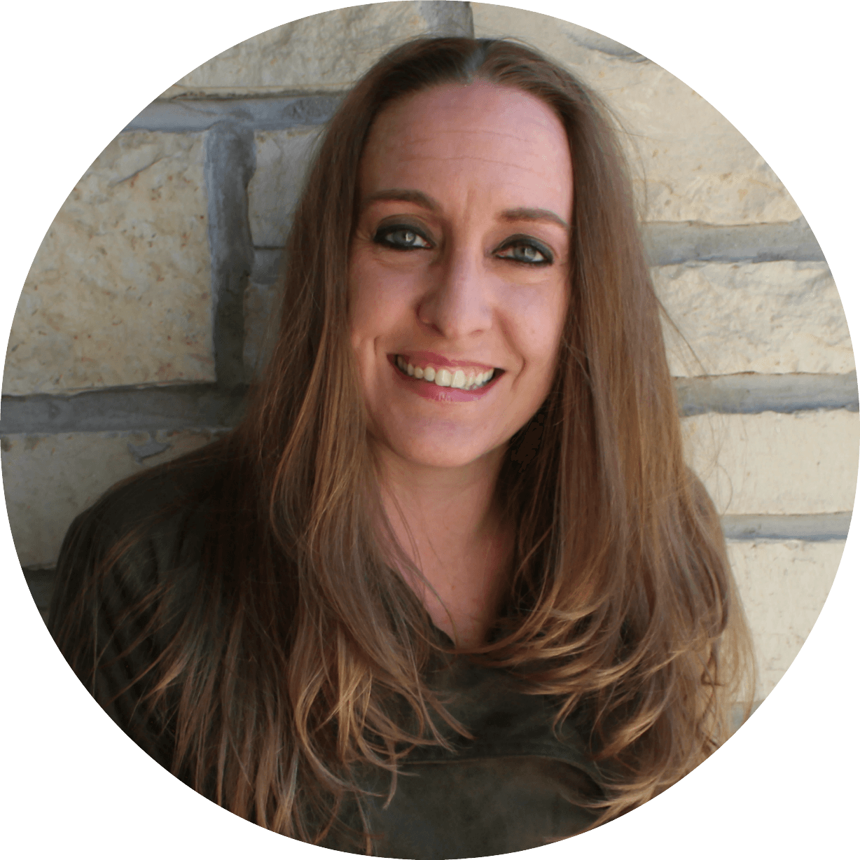 A woman with long brown hair is smiling in front of a stone wall