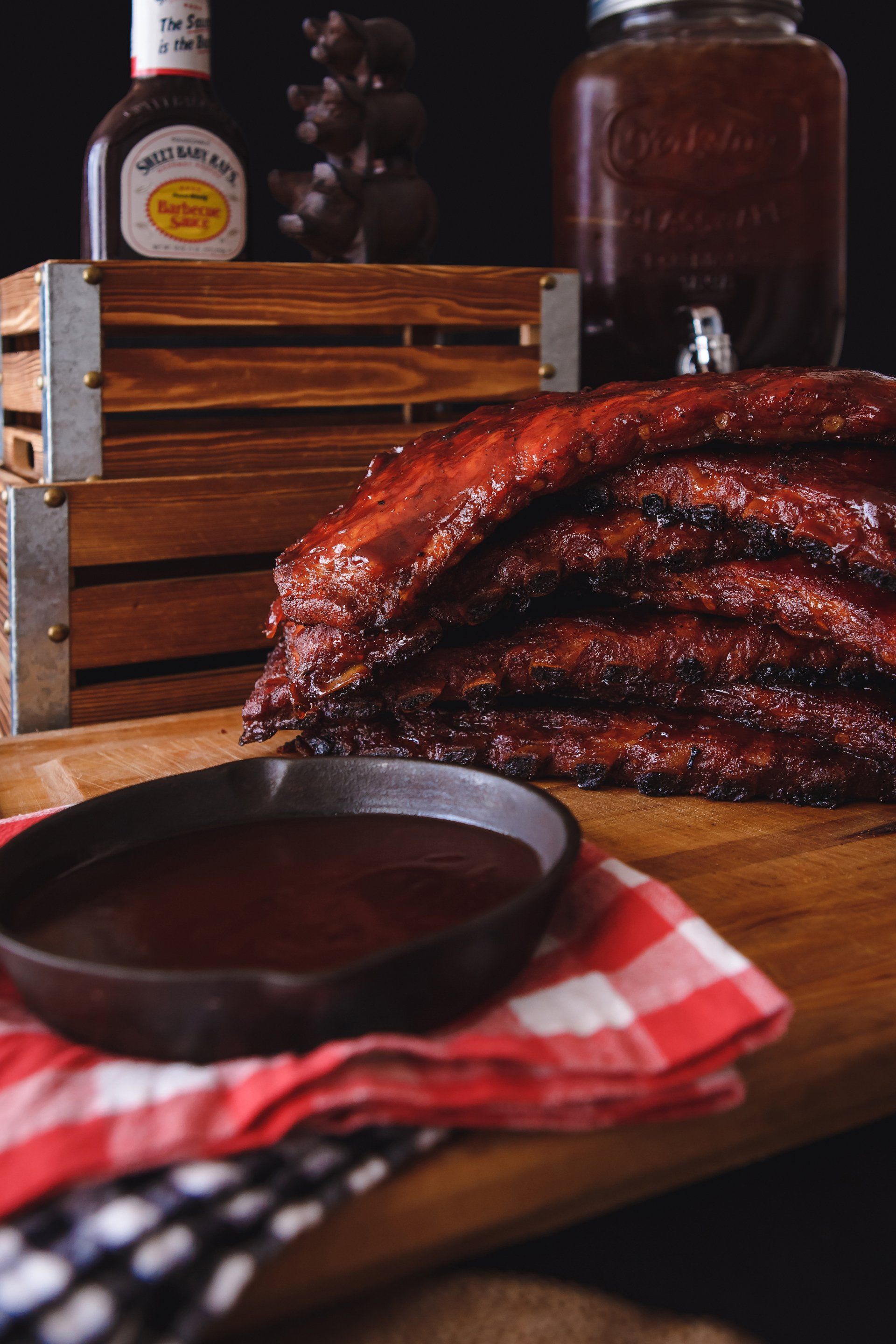 A stack of ribs is sitting on a wooden table next to a bowl of barbecue sauce.