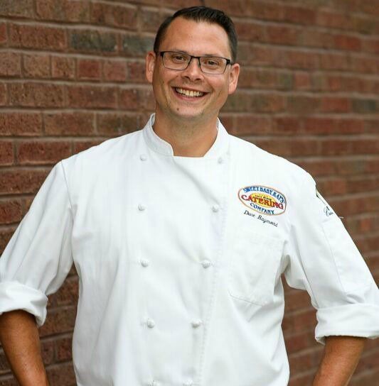 A man wearing a white chef 's jacket with the word capitol on it