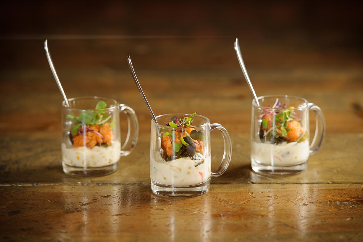 Three glasses filled with food and spoons on a wooden table.