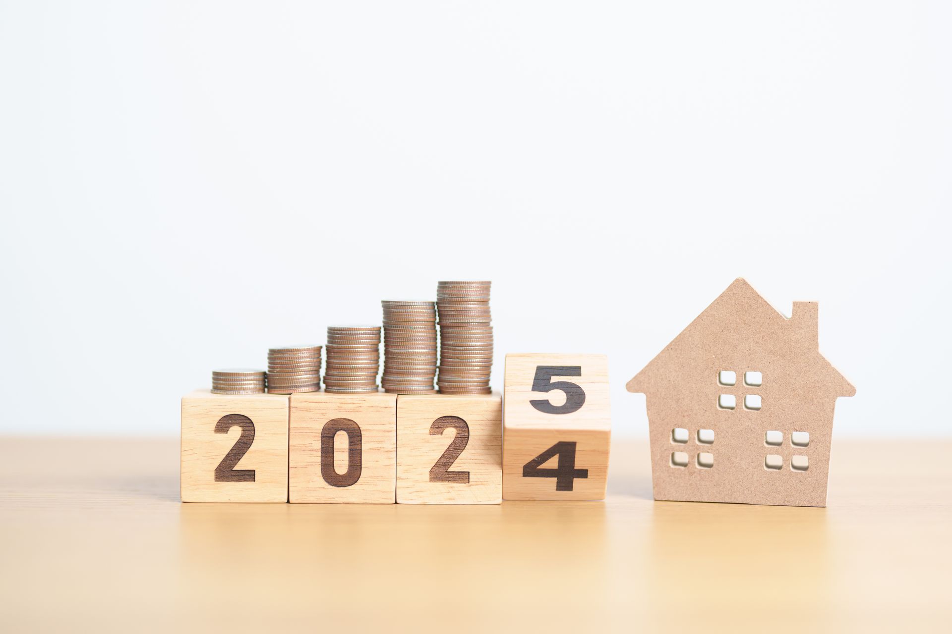 A wooden house and stacks of coins on a wooden table.