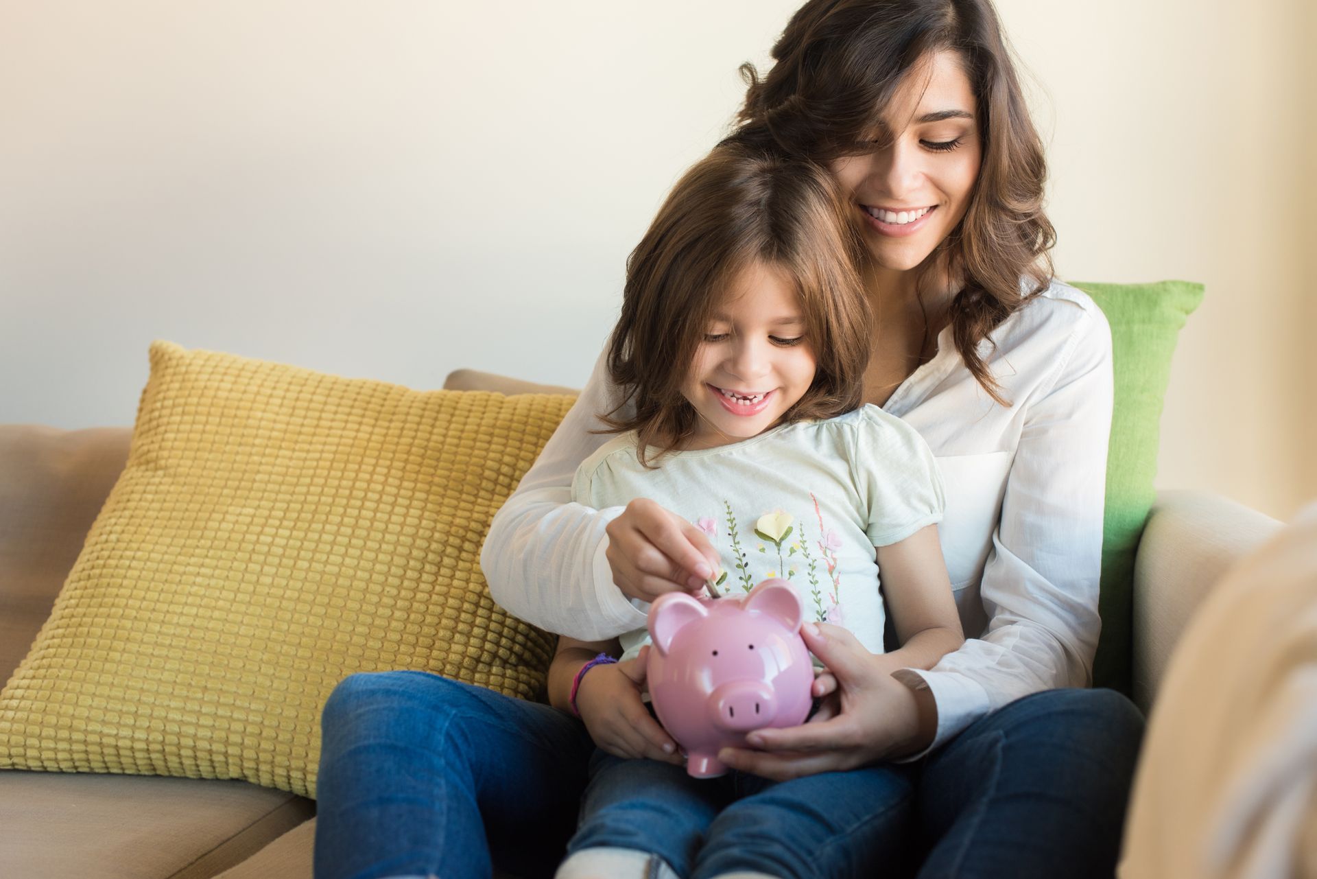 A woman and a little girl are sitting on a couch holding a piggy bank.