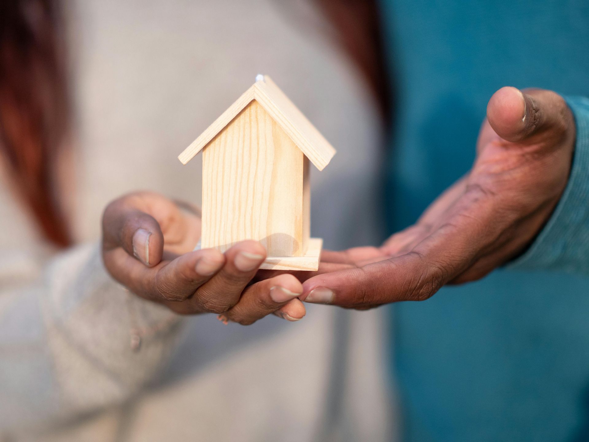 A man and a woman are holding a small wooden house in their hands.