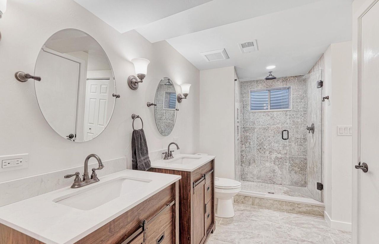 A bathroom with two sinks , a toilet , and a walk in shower.
