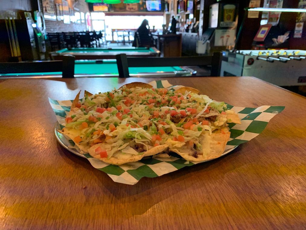 A plate of nachos is sitting on a wooden table in front of a pool table.