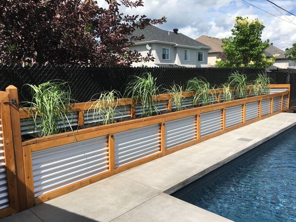 Un muret en bois et en tôle ondulée sépare la terrasse de la piscine de la pelouse du jardin.