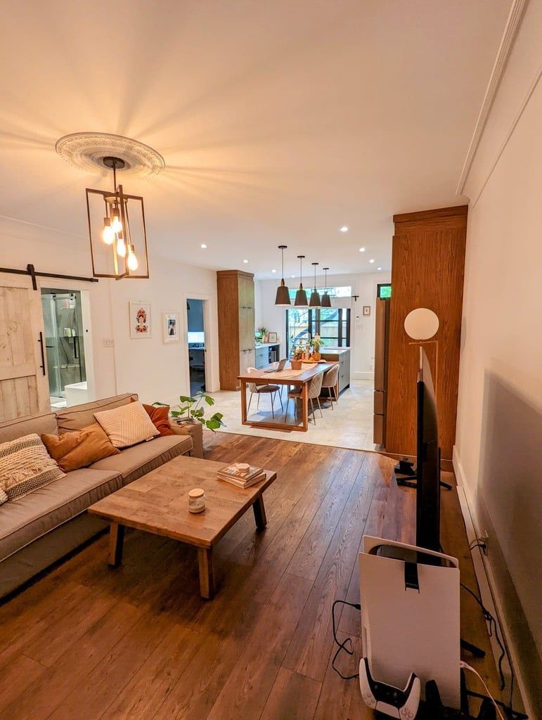 Un espace de vie ouvert comprenant salon et salle à manger, avec parquet, meubles aux tons neutres, table basse en bois et éclairage chaleureux.