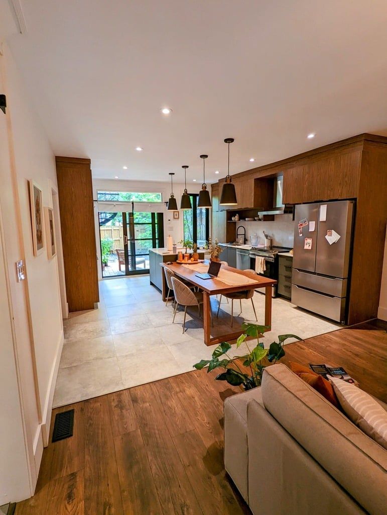 Une cuisine et une salle à manger à aire ouverte comprenant des armoires en bois, une table à manger en bois et des carreaux de sol de couleur claire.