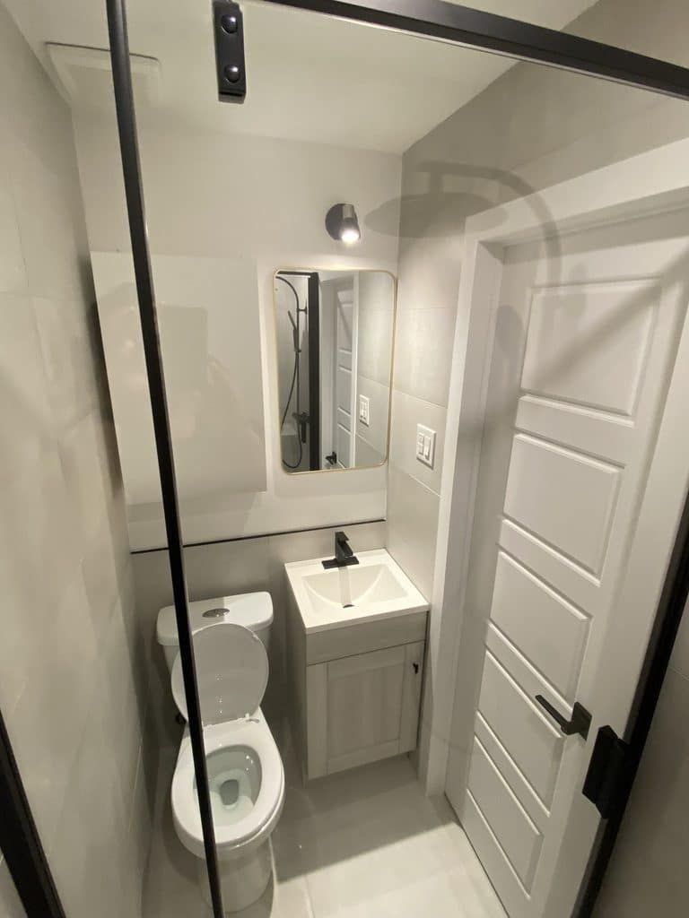 Une petite salle de bains moderne avec des toilettes blanches, un meuble-lavabo gris avec lavabo, un miroir et une porte de douche à cadre noir.