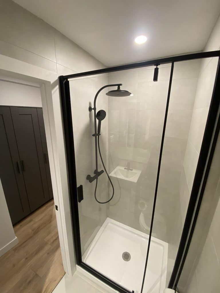 Une cabine de douche moderne en verre avec cadre noir, une pomme de douche effet pluie et une douchette, installée dans une salle de bains.