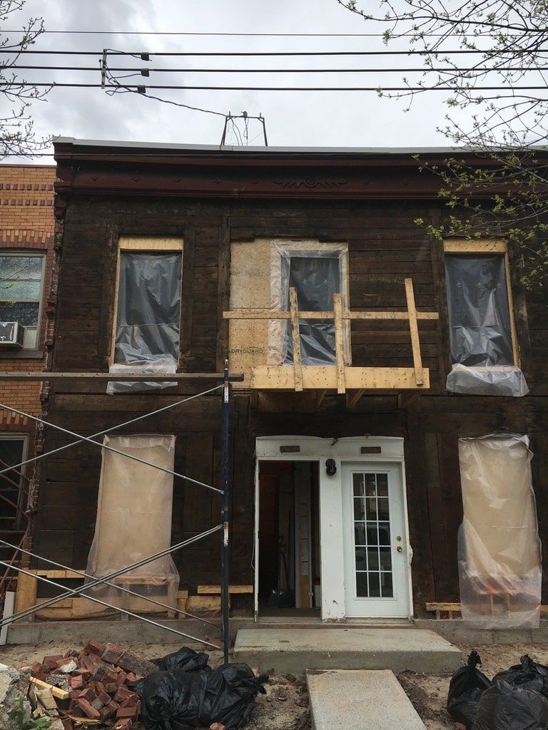 Un bâtiment de deux étages en construction, avec une charpente brun foncé, des protections de fenêtres temporaires et des échafaudages en bois.
