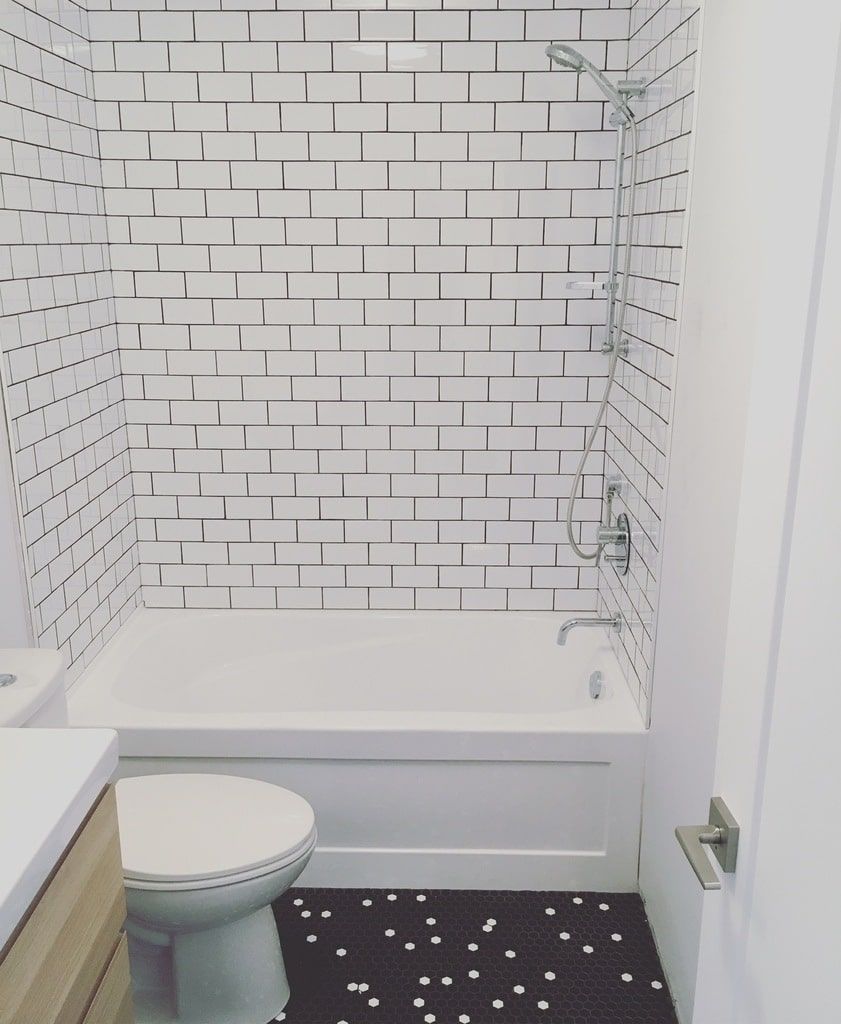 Une salle de bains avec des murs carrelés de carreaux de métro blancs, une baignoire blanche, des toilettes et un sol noir à motifs circulaires blancs.