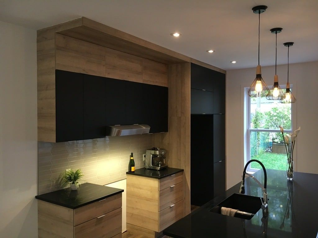 Une cuisine moderne avec des armoires en bois, des comptoirs noirs, des spots encastrés au plafond et trois suspensions lumineuses.