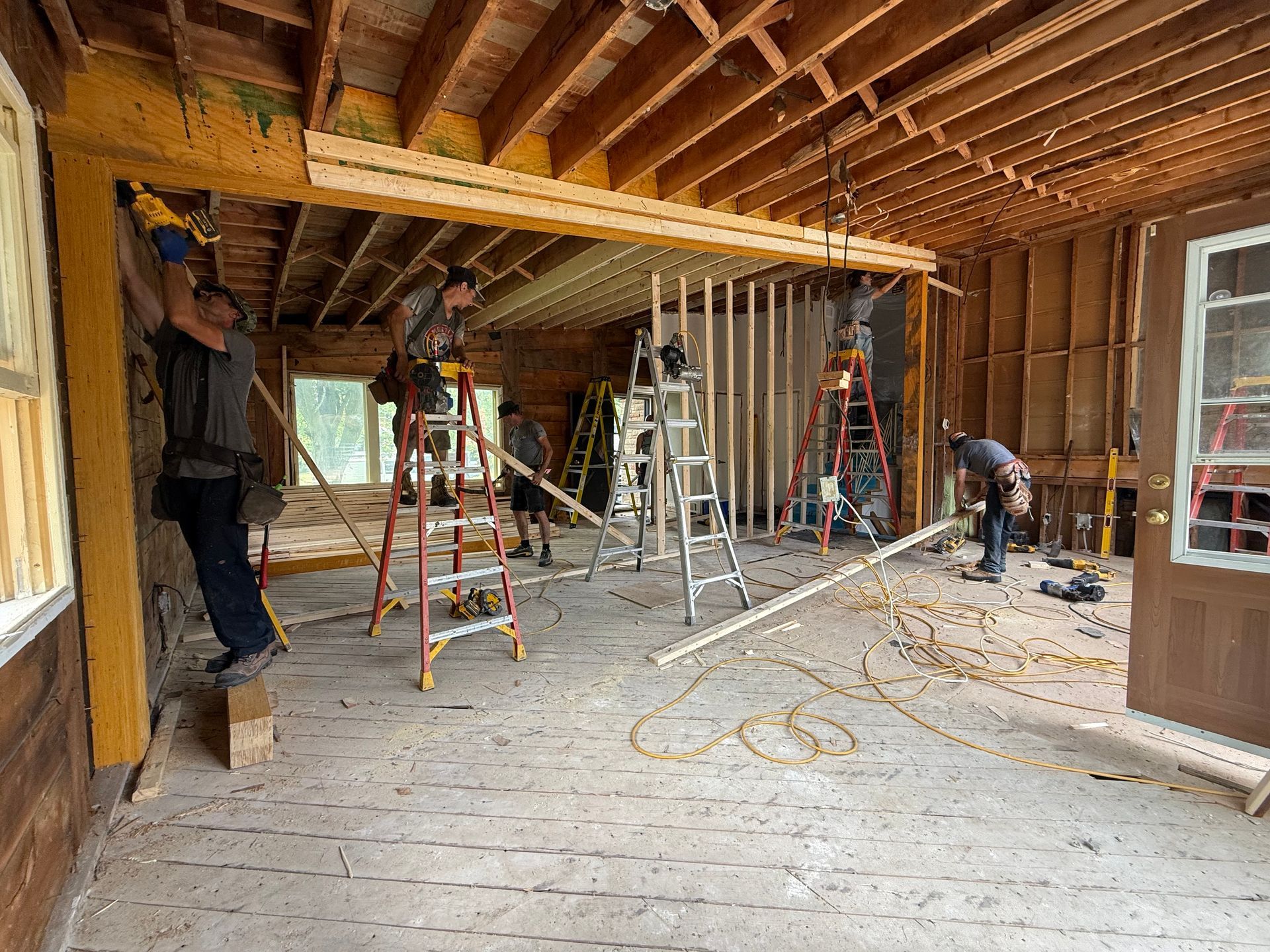 Des ouvriers du bâtiment effectuent des travaux de charpente dans une pièce inachevée dont les poutres de plafond et les montants muraux sont en bois apparent.