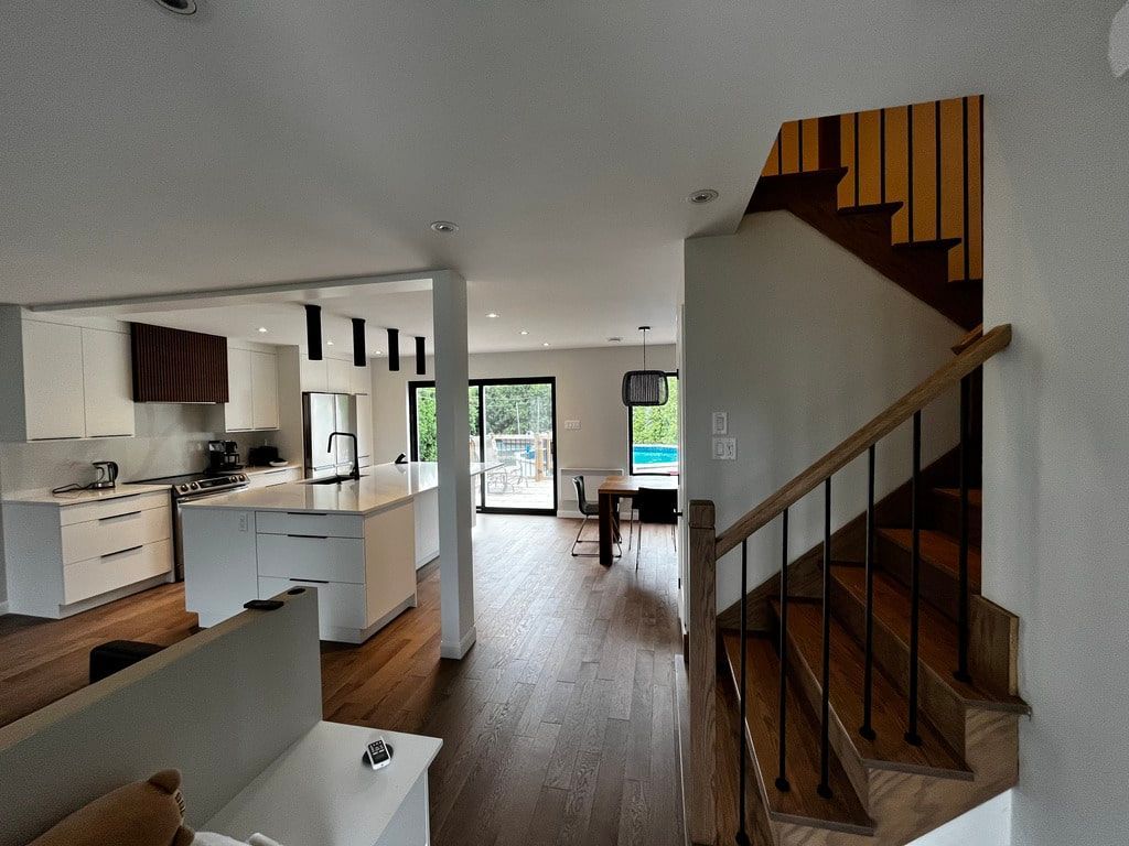 Intérieur d'une maison moderne à aire ouverte comprenant un îlot de cuisine blanc, un parquet et un escalier avec une rampe en bois.