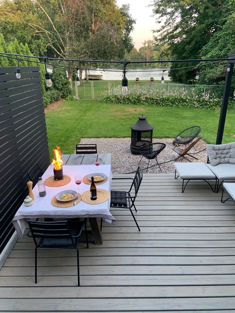 Une terrasse surplombant un lac, avec une table à manger dressée, un centre de table avec une flamme, des chaises de patio et un espace foyer.