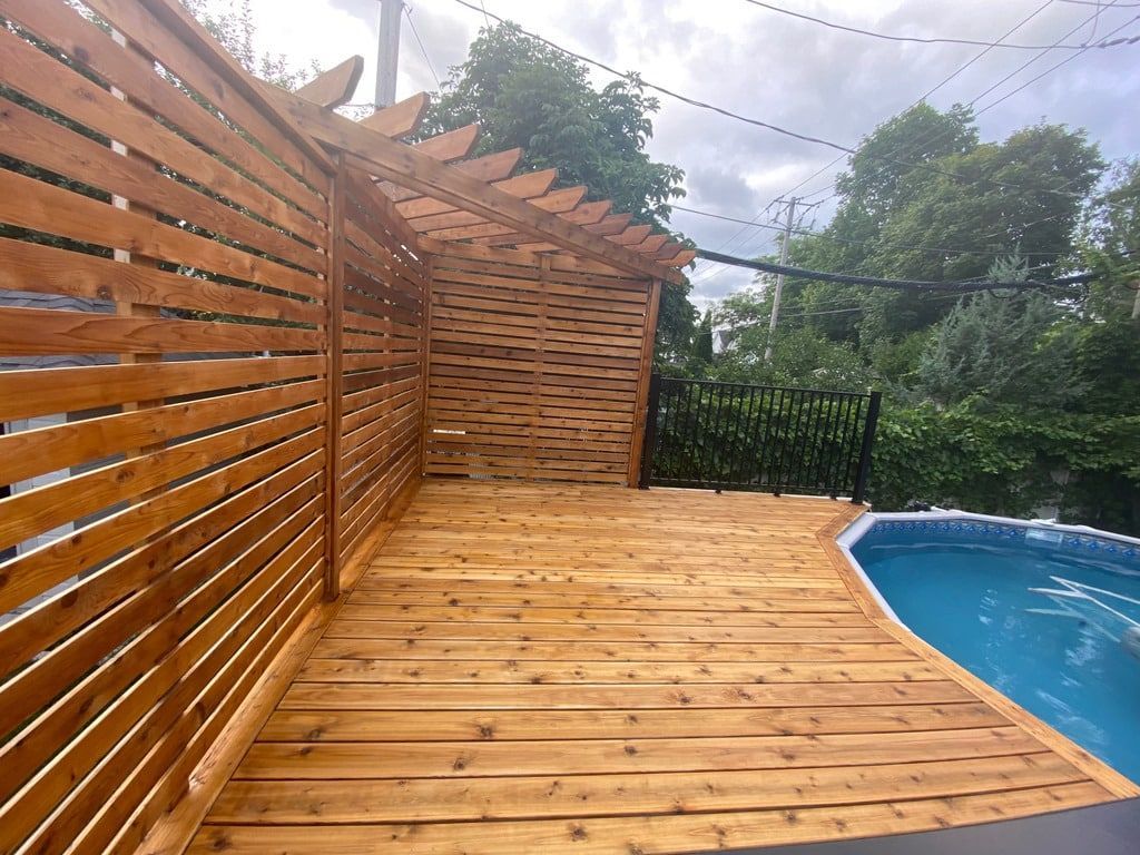 Une terrasse en bois avec un muret d'intimité et une pergola jouxte une piscine hors sol.