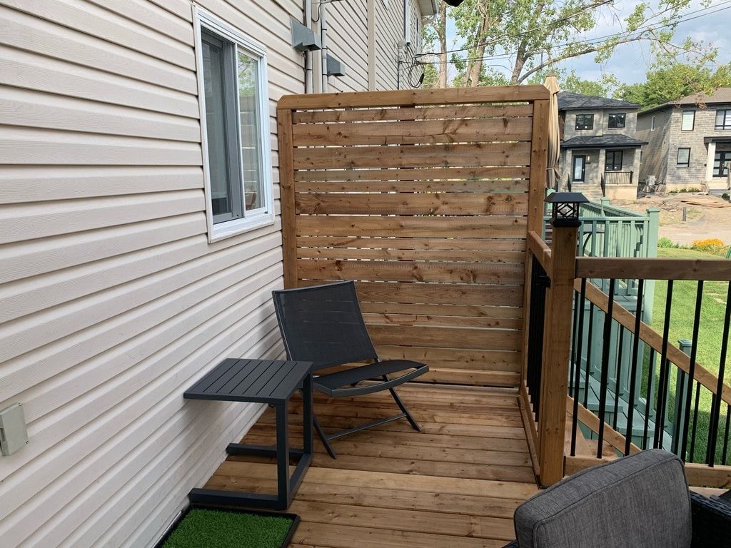 Une terrasse avec un paravent en bois, une chaise sombre et une petite table d'appoint adossée au mur clair d'une maison.