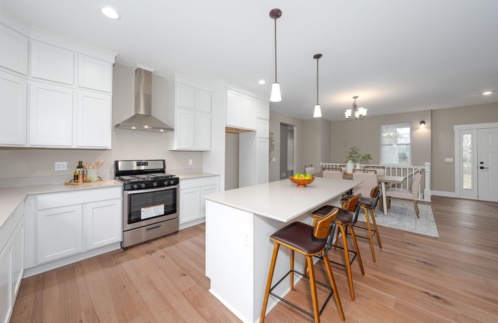 Une cuisine lumineuse avec des armoires blanches, des appareils électroménagers en acier inoxydable, un îlot central avec tabourets de bar et un parquet.