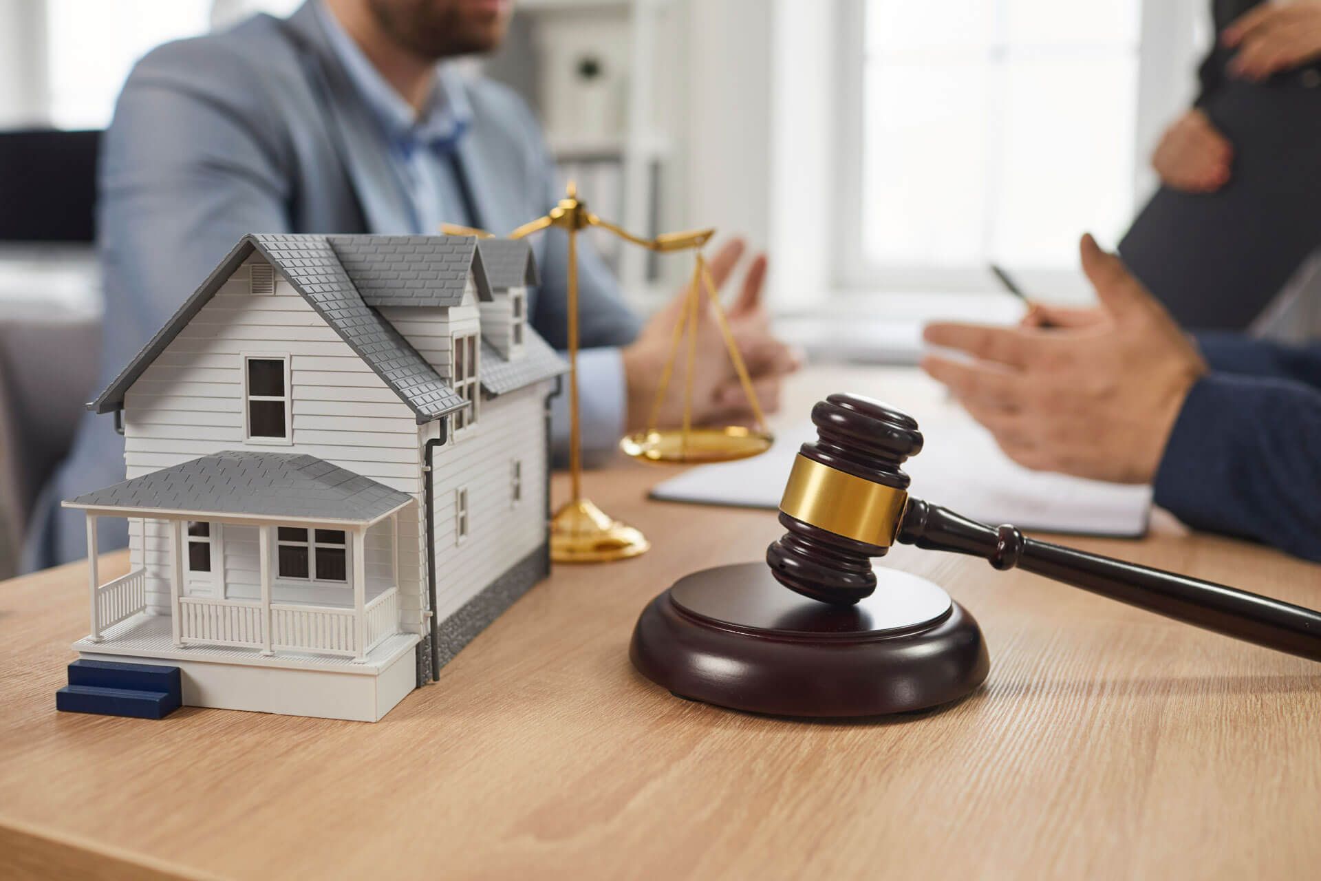 A couple of men are sitting at a table with a model house and a gavel.