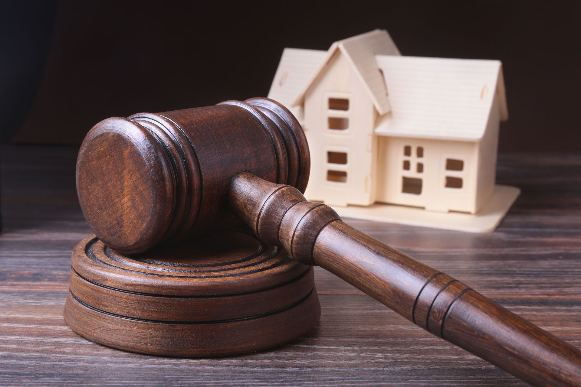 A wooden judge's gavel is sitting on a wooden table in front of a model house.