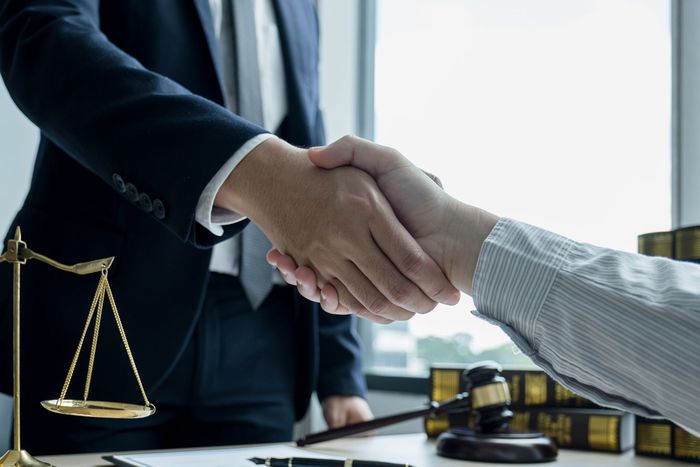 Two men are shaking hands in front of a scale of justice.