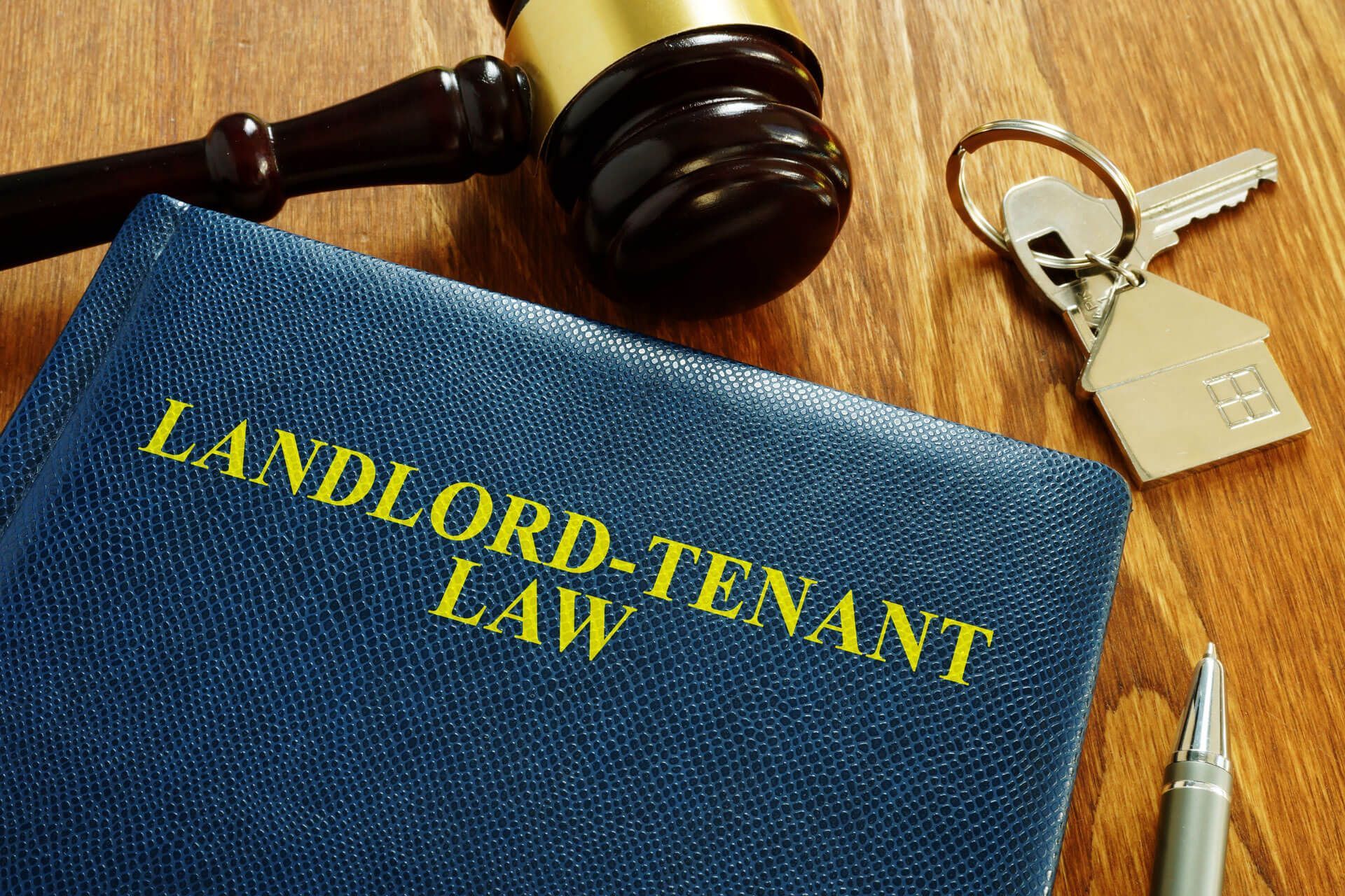 A book titled landlord-tenant law is sitting on a wooden table next to a gavel and keys.