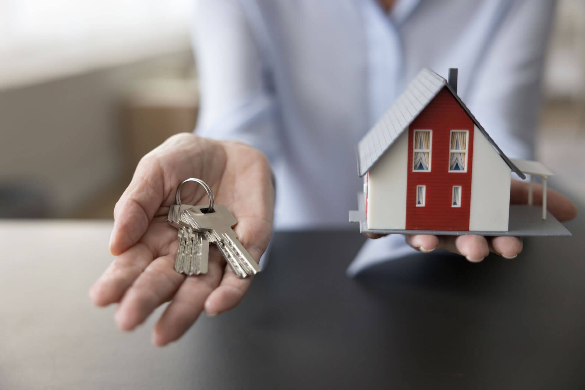 A person is holding a model house and keys in their hands.