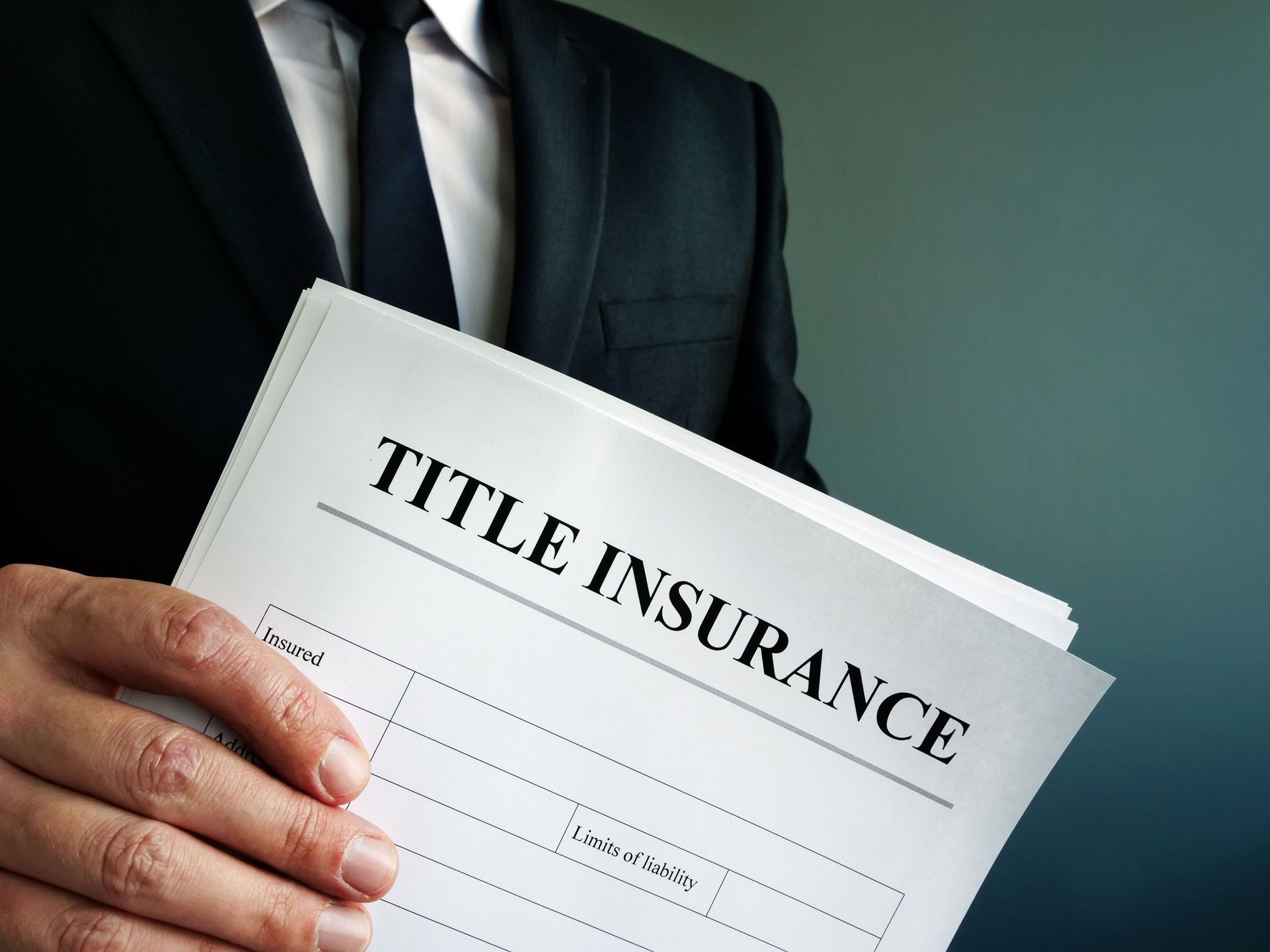 A man in a suit and tie is holding a piece of paper that says title insurance