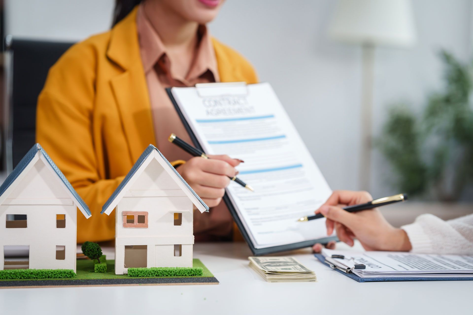 A woman is sitting at a table with two model houses and a clipboard.