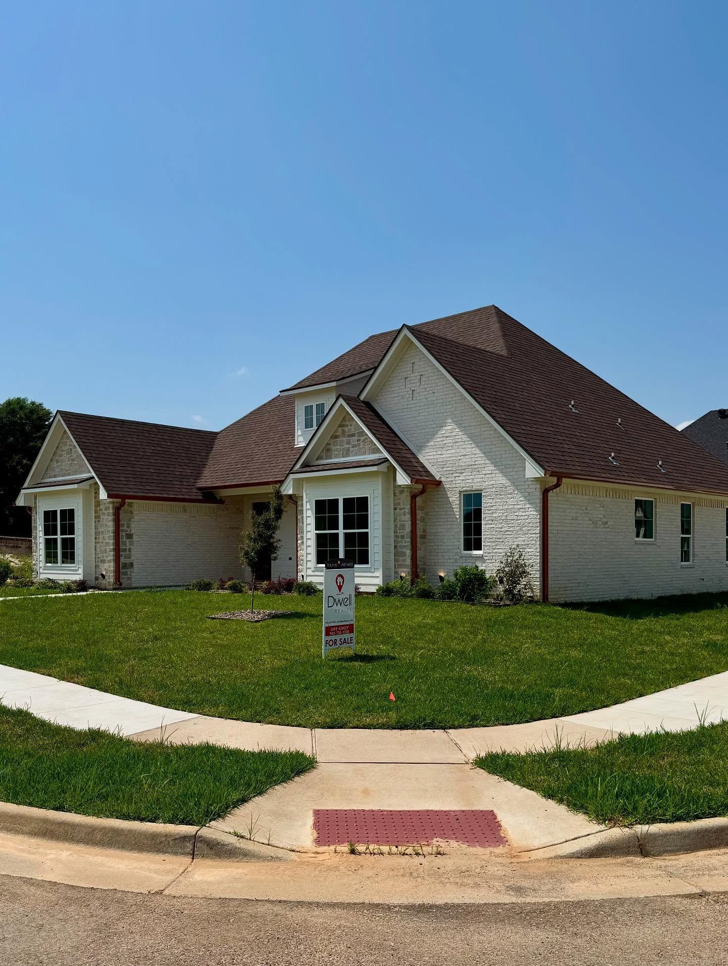 A white house with a brown roof and a for sale sign in front of it.
