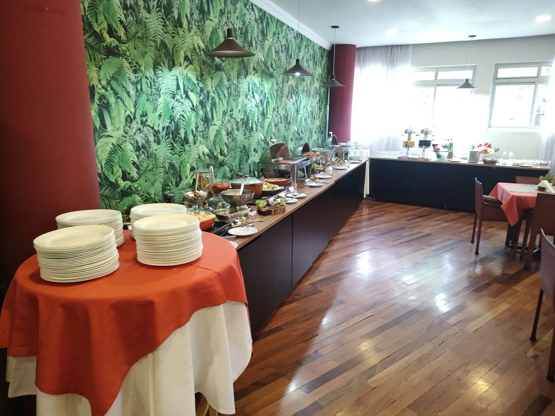 Aparador em uma sala de jantar iluminada com um mural de parede verdejante e piso de madeira polida.