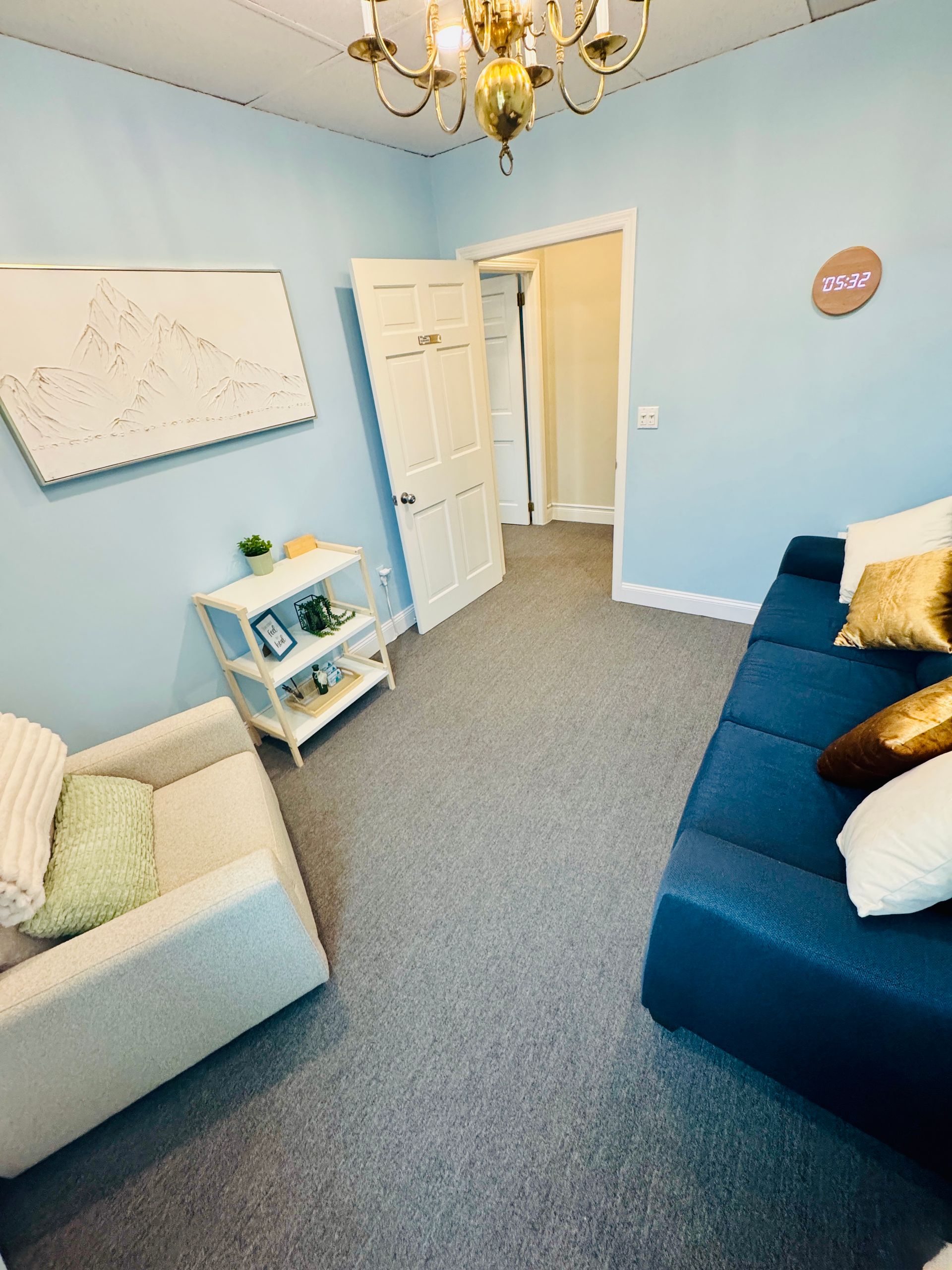 A light blue room with a couch, armchair, shelves, and an open door.