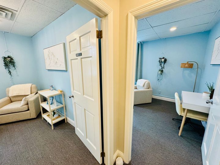 Two therapy rooms: one with a chair and plant, the other with a couch and desk. Blue walls and beige door.