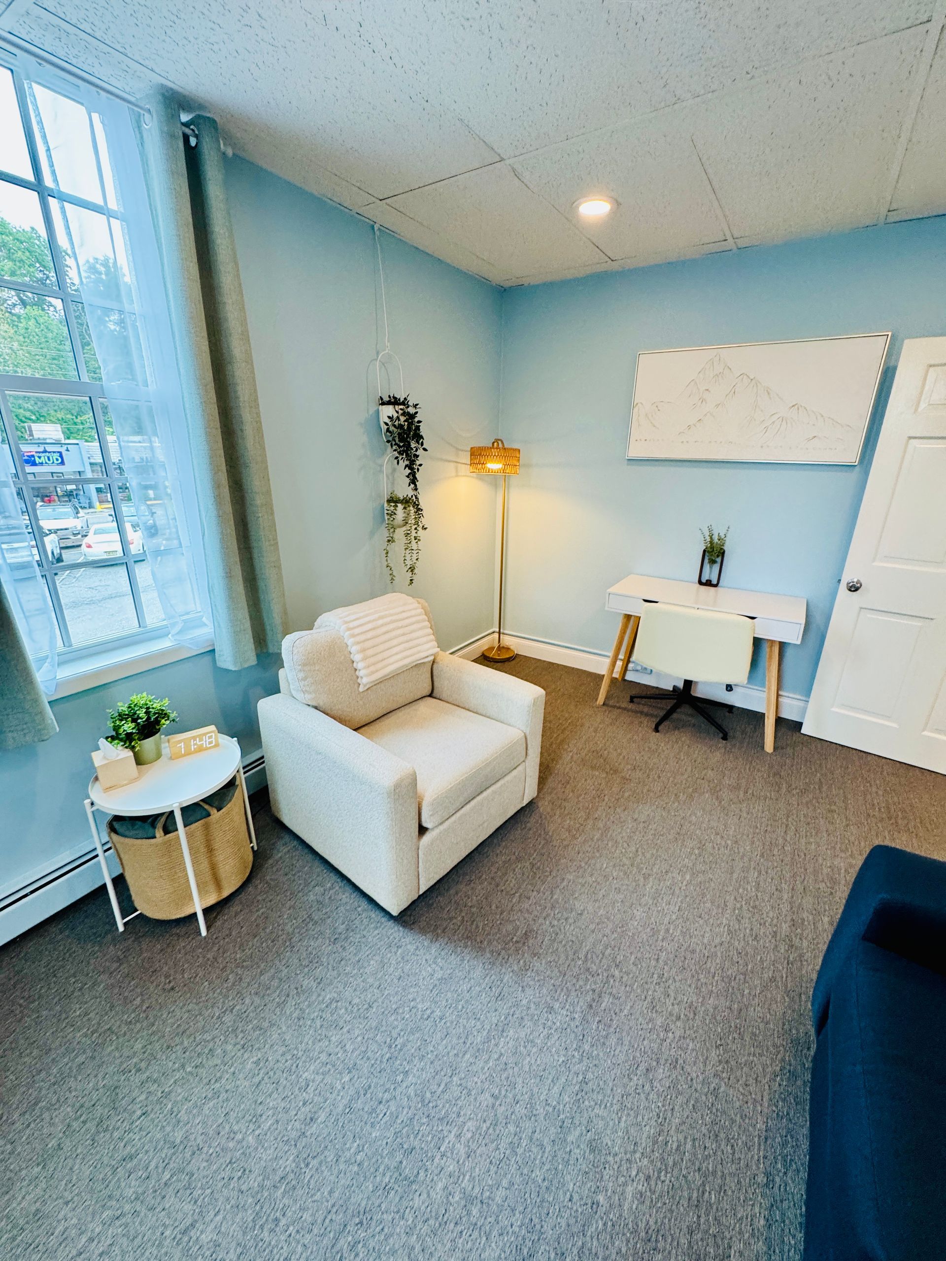 Cozy room with a white armchair, desk, and a window. Light blue walls and carpet.