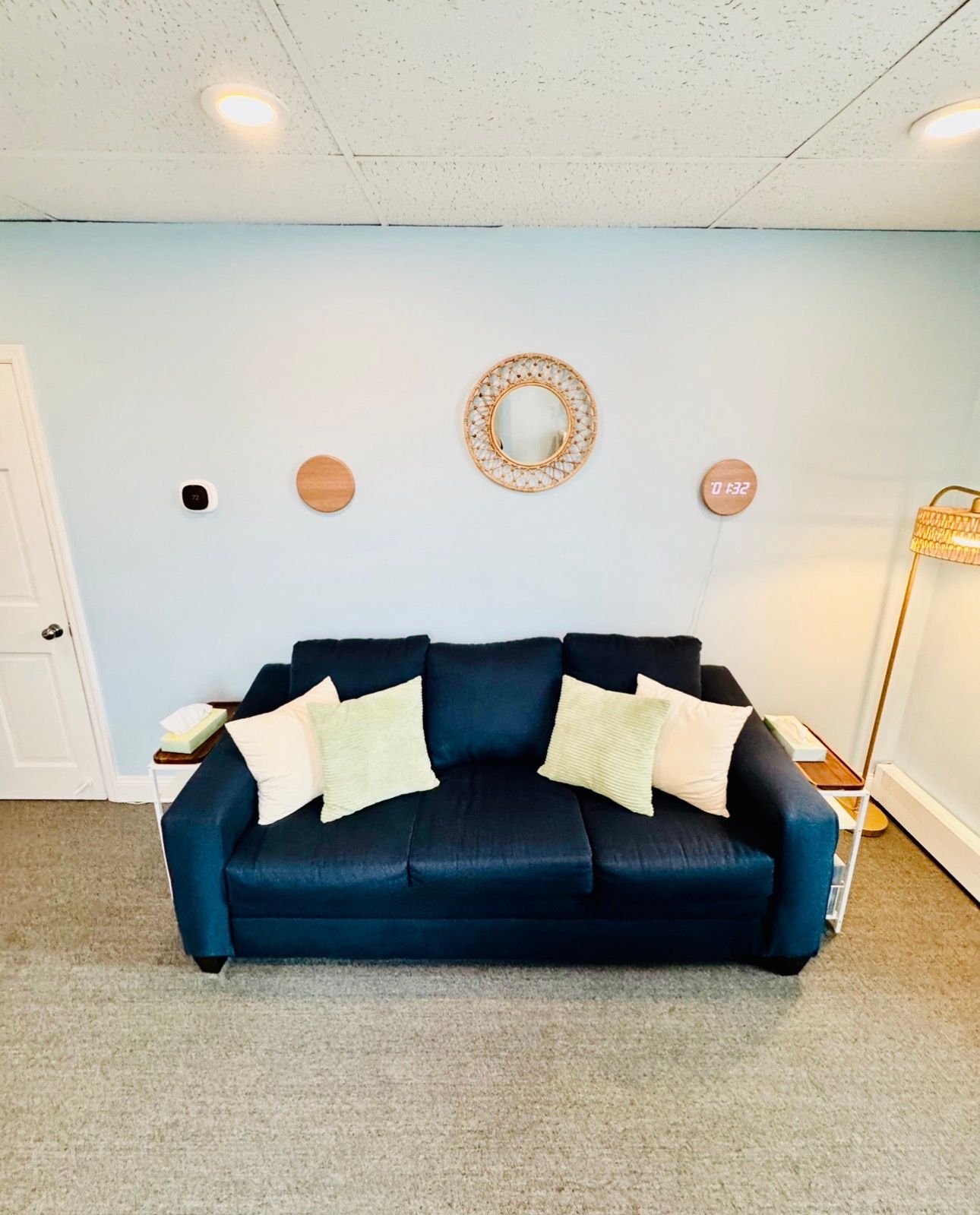 Navy couch with cream and green pillows against a light blue wall. Decor includes wooden circles and a woven wreath.