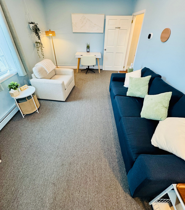 Cozy room with blue walls, a navy sofa with pillows, a white armchair, and a desk.