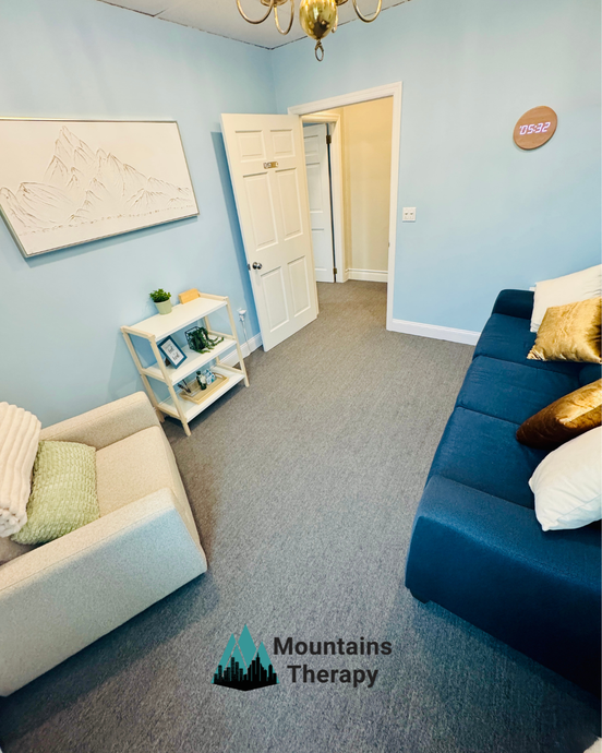 Therapy room with blue walls, sofa, and armchair. Door leads to closet. Mountains Therapy logo.