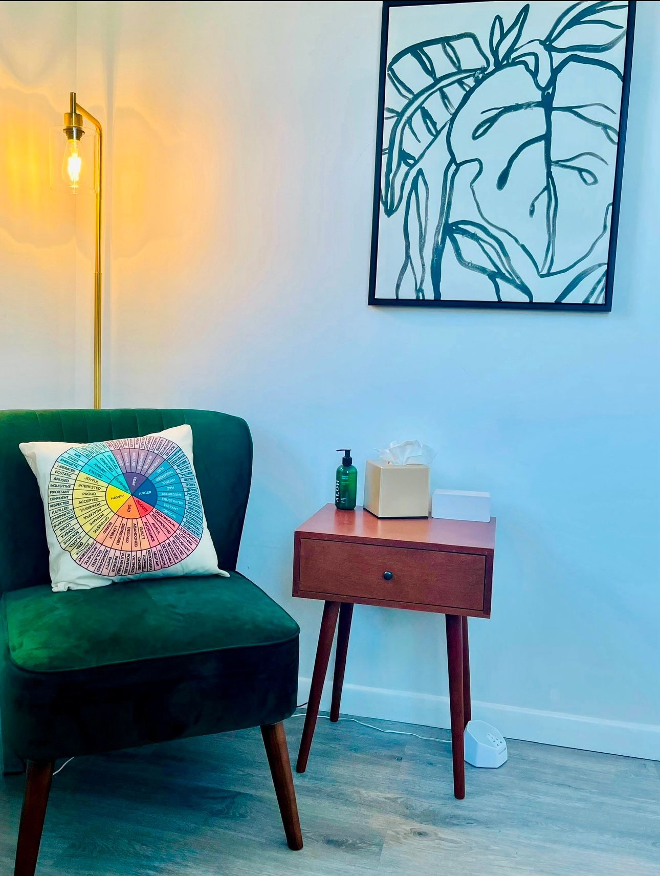 Green armchair with a colorful pillow, next to a wooden table, and a framed botanical print on the wall.