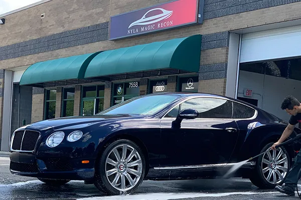 a man is washing a bentley in front of a building .