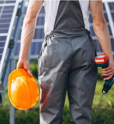 A man in overalls is holding an orange hard hat and a drill