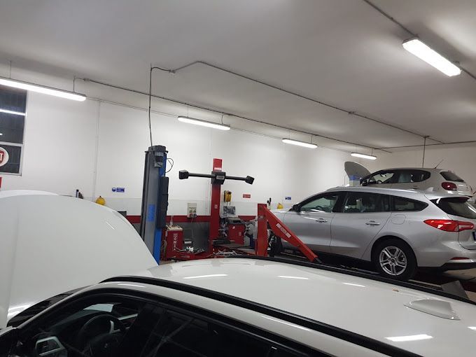 Officina meccanica con un SUV argentato su un ponte sollevatore e un'auto bianca in primo piano.
