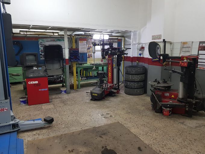 Officina meccanica con ponte sollevatore, pneumatici impilati e attrezzi rossi su un pavimento di cemento.